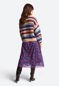 Megzta megčia su kremiškai baltomis, bordo ir mėlynomis juostelėmis, derinama su gėlių raštuotu permatomu sijonu mėlynais ir raudonais atspalviais, vilkima su juodais iki kelių auliniais batais.