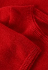 Sarkans vilnas džemperis ar mīkstu tekstūru, ar ribotiem kakla un rokām. Audums izskatās gluds un blīvs.