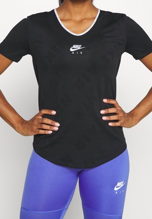 Person trägt schwarzes Nike Air T-Shirt und violette Nike Air Leggings, steht mit Händen in die Hüften vor weißem Hintergrund.