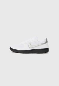 Tênis atléticos brancos com sola de borracha preta, apresentando um swoosh prateado da Nike e detalhes, feitos de materiais têxteis e sintéticos.