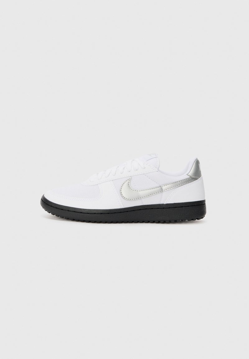 Tênis atléticos brancos com sola de borracha preta, apresentando um swoosh prateado da Nike e detalhes, feitos de materiais têxteis e sintéticos.