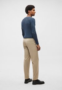 Bordázott tengerészkék pulóver és bézs nadrág, oldalnézet. A pulóver hosszú ujjú; a nadrág oldalzsebes és egyenes szárú. Fekete cipő.