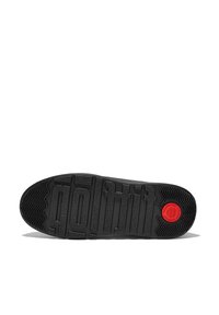 Suela de zapatilla negra con surcos profundos para tracción, superficie texturizada y un prominente logo circular rojo. Diseño plano y ancho para estabilidad.
