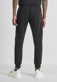 Zwarte trainingsbroek met een elastische tailleband, zijzakken en ribgebreide boorden, evenals een gladde, zachte textuur. Draagt met witte sneakers.