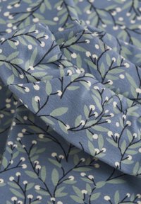 Tissu bleu avec un motif botanique présentant des feuilles vertes et des baies blanches sur des branches noires ; texture lisse et design léger.