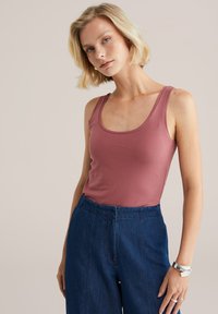 Top sin mangas burdeos ajustado con escote redondeado, tejido suave y tirantes finos, combinado con pantalones de mezclilla azul de tiro alto.