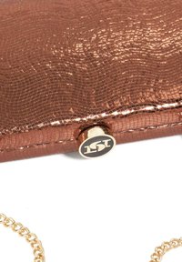 Rose gold, textured clutch purse with a crocodile pattern, gold hardware, and a circular logo button. Features a detachable gold chain strap.