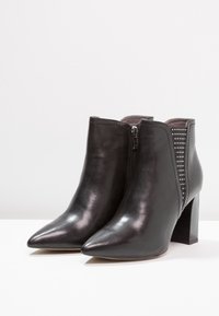 Botas de tobillo de cuero negro con punta afilada, cremallera lateral y acentos de malla perforada, que cuentan con un tacón bloque apilado.