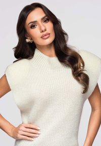 Pull en maille ivoire avec col montant, manches courtes et tissu texturé. Présente une silhouette ajustée et des détails subtils.