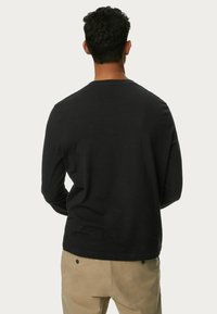 Sort langærmet skjorte lavet af blødt stof, med en klassisk rund hals og enkelt design, vist mod en neutral baggrund.