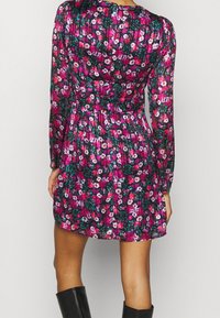 Kukkakuosisessa mekossa tummassa kankaassa on kirkas vaaleanpunaisen ja valkoisen kukkakuosi. Pitkät hihat ja vyötäröltä kiristetty malli, jossa on takana suljettavat napit.