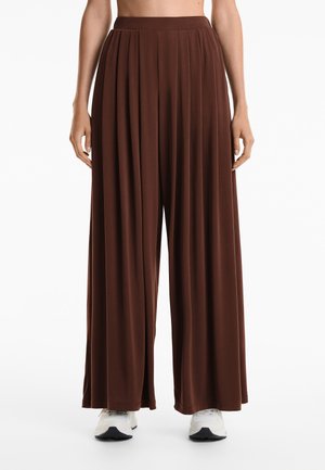 Bruine wijde broek met een geplooid ontwerp, gemaakt van een zachte stof. Heeft een hoge, elastische tailleband en valt tot de enkels.