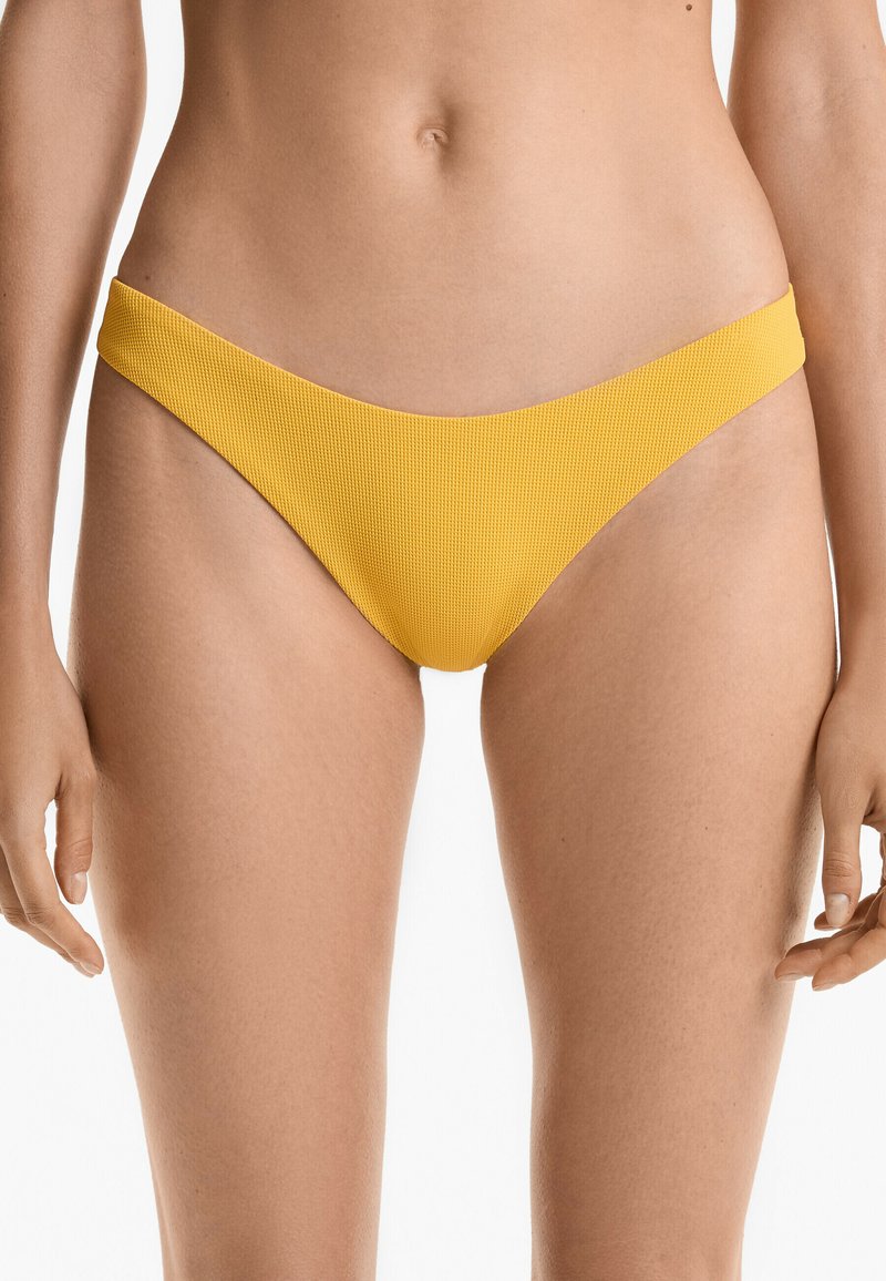 Gula bikiniunderdelar med ribbad textur, minimalistisk design och slät midja, visade mot en neutral bakgrund.