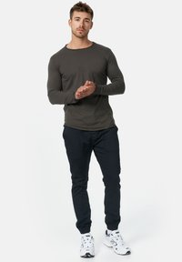 Camisa de manga larga gris oscuro con cuello redondeado, combinada con pantalones negros ajustados y zapatillas blancas con detalles en negro.