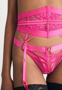 Rosa sateng undertøysett med strukturert blonderdesign, meshpaneler, glidelåsdetaljer, og justerbare stropper med gullfarge.