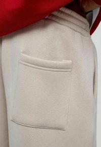 Lichtbeige sweatpants hebben een gestikte achterzak en een elastische tailleband, met een zichtbare naaddetails en een zachte textuur.