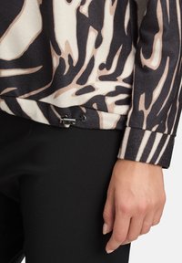 Langsleeve top in een beige en zwart dierenprint, geribbelde textuur, met zwarte accentstiksels en een horizontale streepdetail op de mouwen.