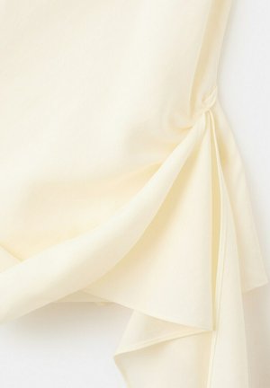 Kermansävyistä läpikuultavaa kangasta, joka on laskostettu ja sidottu löyhäksi solmuksi, luoden kerroksellisia taitoksia ja pehmeän tekstuurin valkoista taustaa vasten.