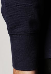 Marineblauer Sweatshirt-Manschette mit einer strukturierten Oberfläche, die am Boden über ein geripptes Strickmuster und darüber eine glatte Stoffoberfläche verfügt.