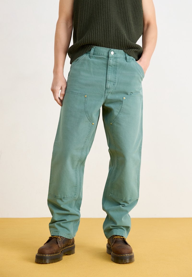 Ljusgröna vida byxor med stora sidofickor, metalldetaljer och sydda detaljer, kombinerade med bruna snörstövlar.