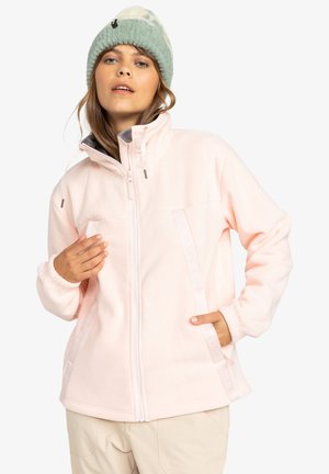 Lichtroze fleecejack met een volledige rits, voorzien van bandaccenten en elastische boorden. Het model draagt een mintgroene beanie met patroon.
