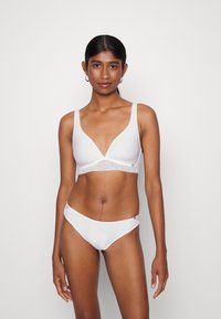 Balta liemenėlė su giliu V-ksiu, minkšta medžiaga ir nėrinių apdaila juostoje. Atitinkamos baltos bikini kelnaitės su lygiu paviršiumi. Minimalistinis dizainas.