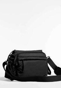 Črna torba za sporočila z oblazinjenim vzorcem, več zaprtih predelkov z zadrgami, nastavljivim trakom in ravno površino za stabilnost.