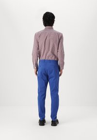 Camisa de cuadros para hombre en rojo y blanco, con cuello, combinada con pantalones azules. La tela parece suave, con un corte ajustado.