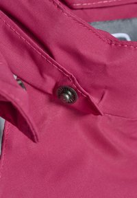 Rosa tyg med en slät textur, med en metallisk tryckknapp och sömnadsdetaljer. Fokuserar på plaggets konstruktion.