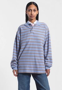 Blå långärmad pikétröja med horisontella bruna ränder, utrustad med krage och avslappnad passform. Tyget har en texturerad yta.