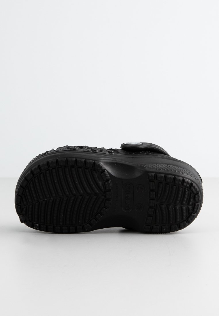 Zwarte schoenen met een gestructureerde rubberen zool, voorzien van een sluiting met een band en een geribbelde patroon voor grip. Glad bovenwerk met subtiele details.