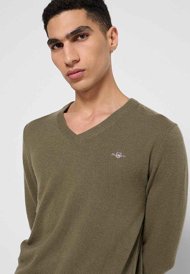 Olivgrön V-ringad tröja i ett strukturerat stickat tyg, med en liten logotyp på vänster bröst och en avslappnad passform.