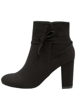 Sort ankelstøvle i ruskind med blokhæle, rundet tå og dekorativ bindedetalje omkring siden.