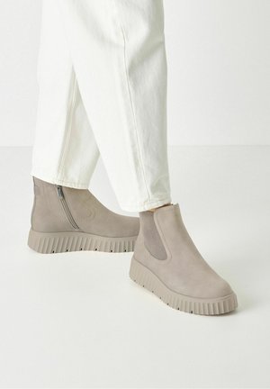 Lyse beige platform-ankelstøvler med teksturerede såler, elastiske sidepaneler og lynlåse, båret med hvide bukser.