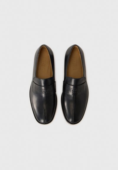 Chaussures noires en cuir à enfiler avec une finition lisse et des détails cousus. Présentent une semelle plate et un design avant distinct.