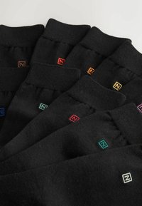 Siedem par czarnych skarpet ułożonych obok siebie, każda z małym kolorowym kwadratowym logo z literą "N" blisko mankietu.