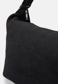 Bolsa de ombro em cordura preta, com uma superfície texturizada e estriada, apresentando um fecho de zip e uma alça resistente.