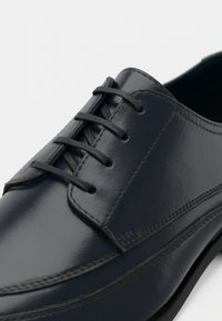 Navy blue leather dress shoe with closed lacing, detailed stitching, and polished finish on a white background.