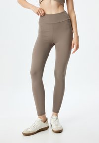 Bruine high-waisted leggings gemaakt van rekbaar materiaal, met een gladde textuur, aansluitend ontwerp en naadloze constructie.