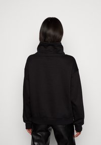Sudadera negra de gran tamaño con cuello alto, mangas largas y dobladillo acanalado. Fabricada con una tela suave de textura lisa.
