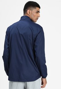 Veste légère bleu marine avec un col haut, des poignets élastiques et une texture lisse, vue de l'arrière.