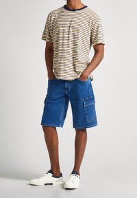 Randig bomullst-shirt i beige och marinblå, i kombination med blå denim cargo-shorts med sidofickor, bärs med vita sneakers.