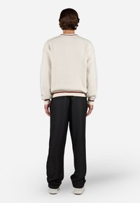 Elfenbensfarvet sweater med tekstureret overflade, ribbede manchetter og kant samt en kontrasterende maroonstribe. Parret med løse sorte bukser og hvide sneakers.