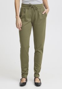 Olijfgroene taps toelopende broek van zacht materiaal, voorzien van een trekkoord in de taille, zijzakken en een gladde textuur.