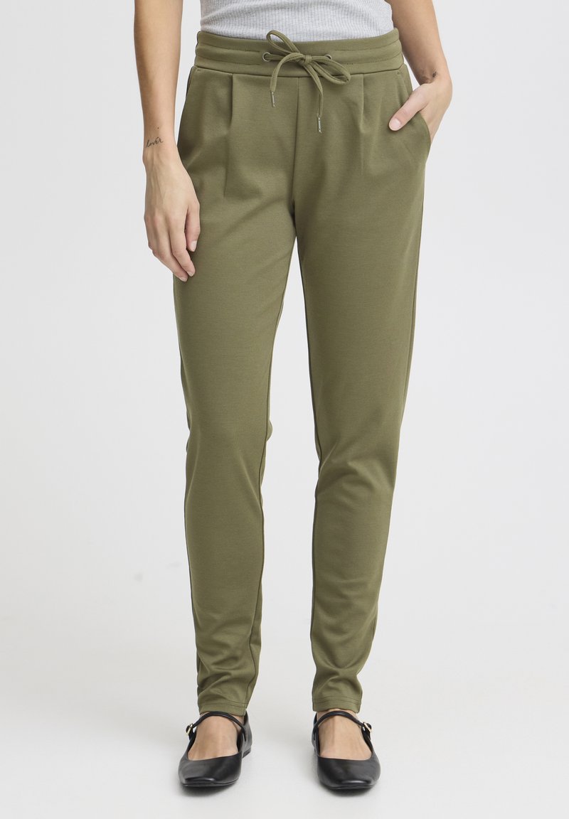 Olijfgroene taps toelopende broek van zacht materiaal, voorzien van een trekkoord in de taille, zijzakken en een gladde textuur.