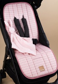 Vaaleanpunainen pehmustettu makuupehmuste, jossa pieni kukkakuosi, musta lastenvaunun runko ja pehmeä vaaleanpunainen pupulelu istuimella.