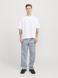 Camiseta blanca de algodón de gran tamaño con mangas cortas, combinada con jeans rectos de color azul claro y zapatos de plataforma negros. Fondo liso.