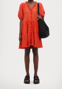 Czerwona bawełniana sukienka z krótkimi bufkami, detalami falbanek i koronkowymi akcentami. W połączeniu z czarną plecioną torebką oraz masywnymi platformami na sandałach.