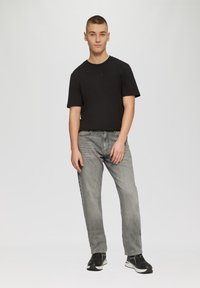 T-shirt noir à manches courtes, jean gris coupe décontractée et chaussures de sport noires. Design simple et palette de couleurs neutres avec un look décontracté.
