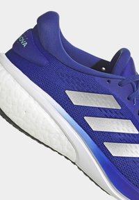 Blue athletic shoe with a textured knit upper, silver stripes on the side, and a white cushioned sole. Features additional blue accents.